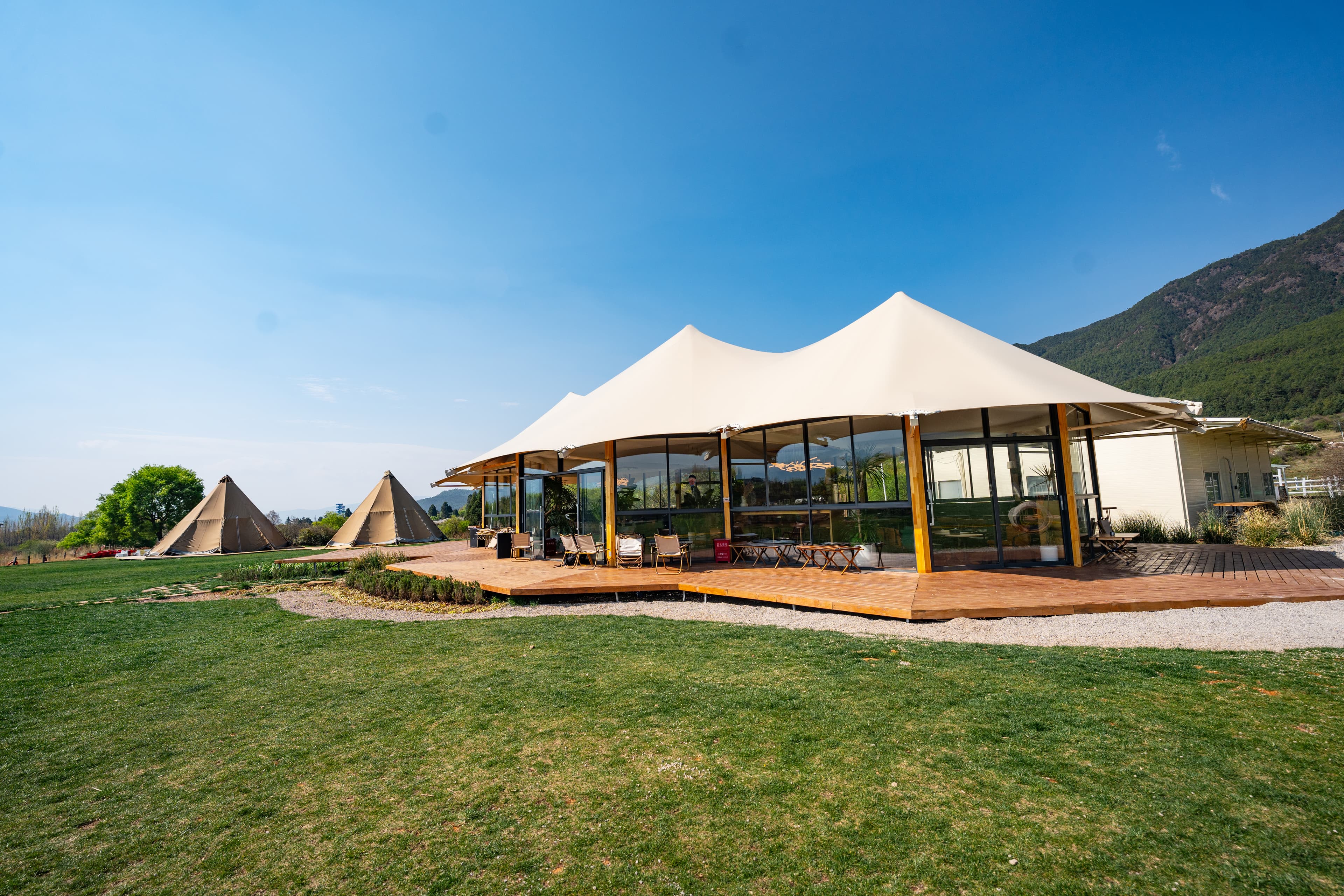 Glamping site featuring a glass-walled pavilion with a canopy roof and teepee tents nearby.