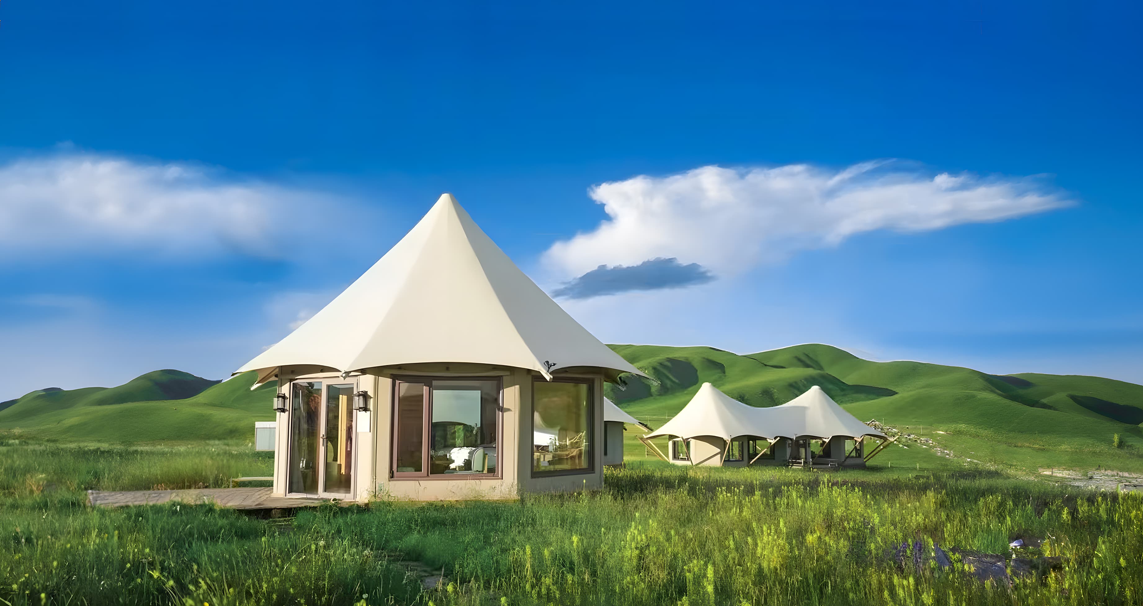 Modern glamping tents with glass windows in a lush green meadow under blue skies.