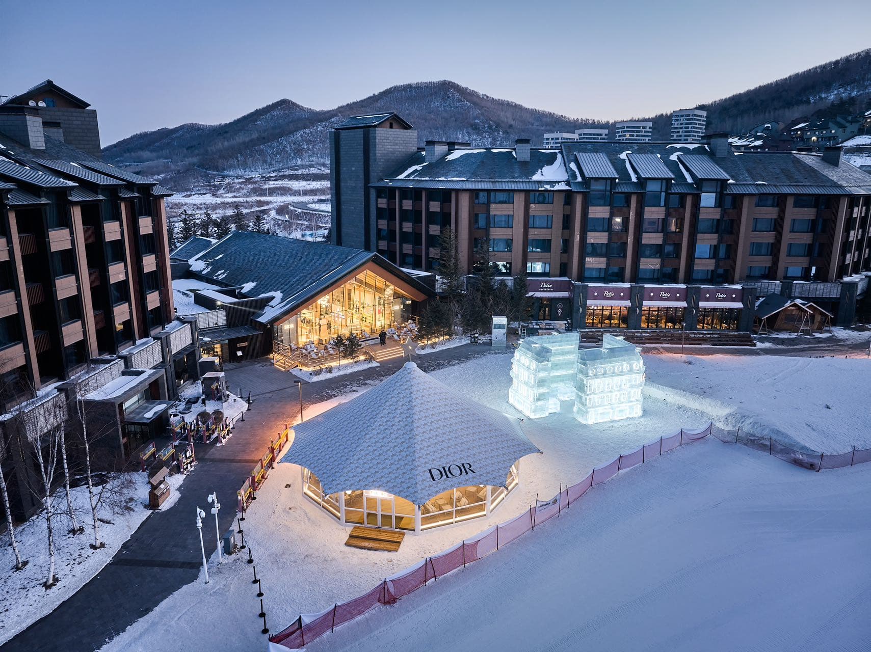 Dior tent and illuminated ice sculptures at a snowy mountain resort during twilight.