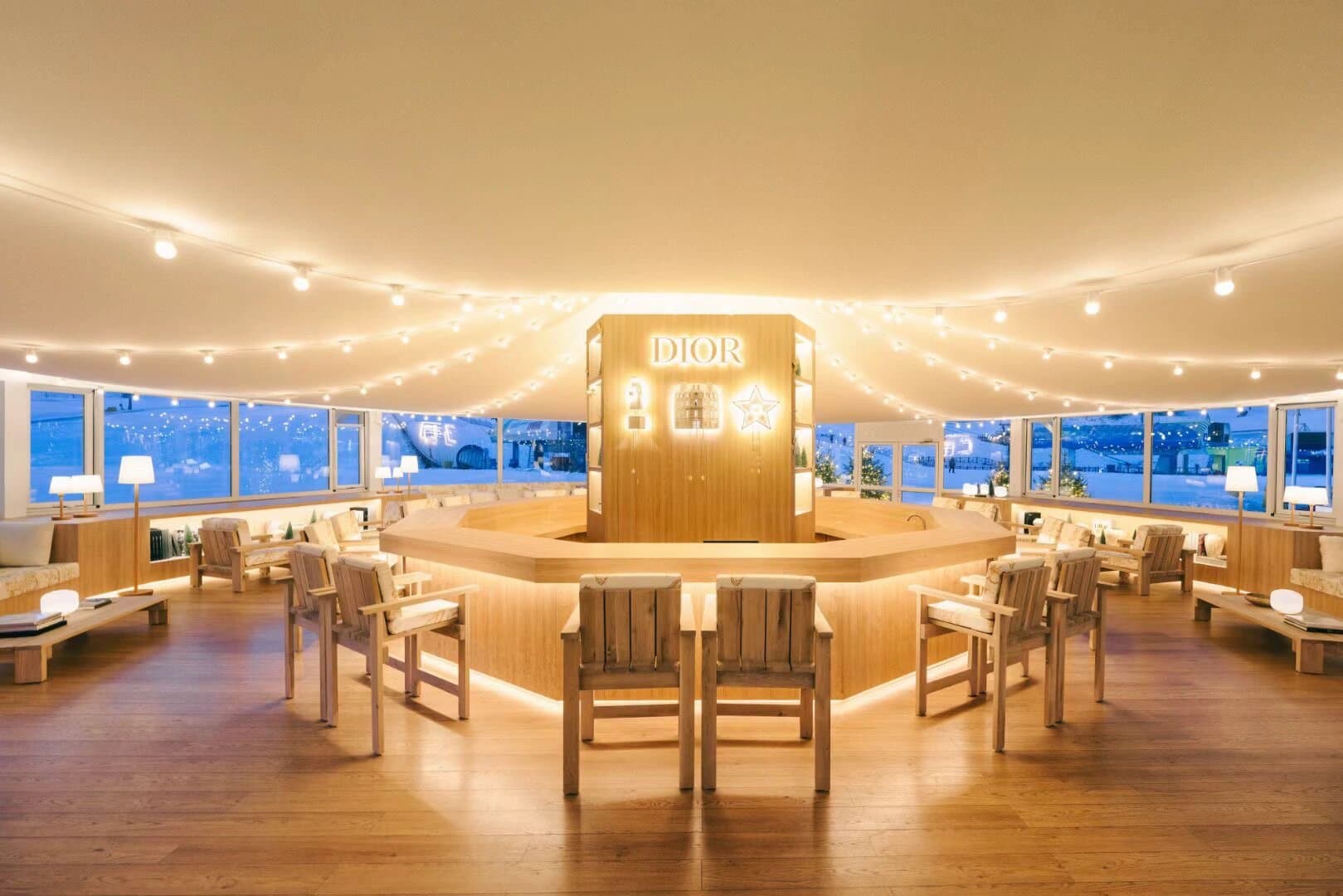 Luxurious Dior lounge with a circular wooden bar, warm lighting, and snowy mountain views.