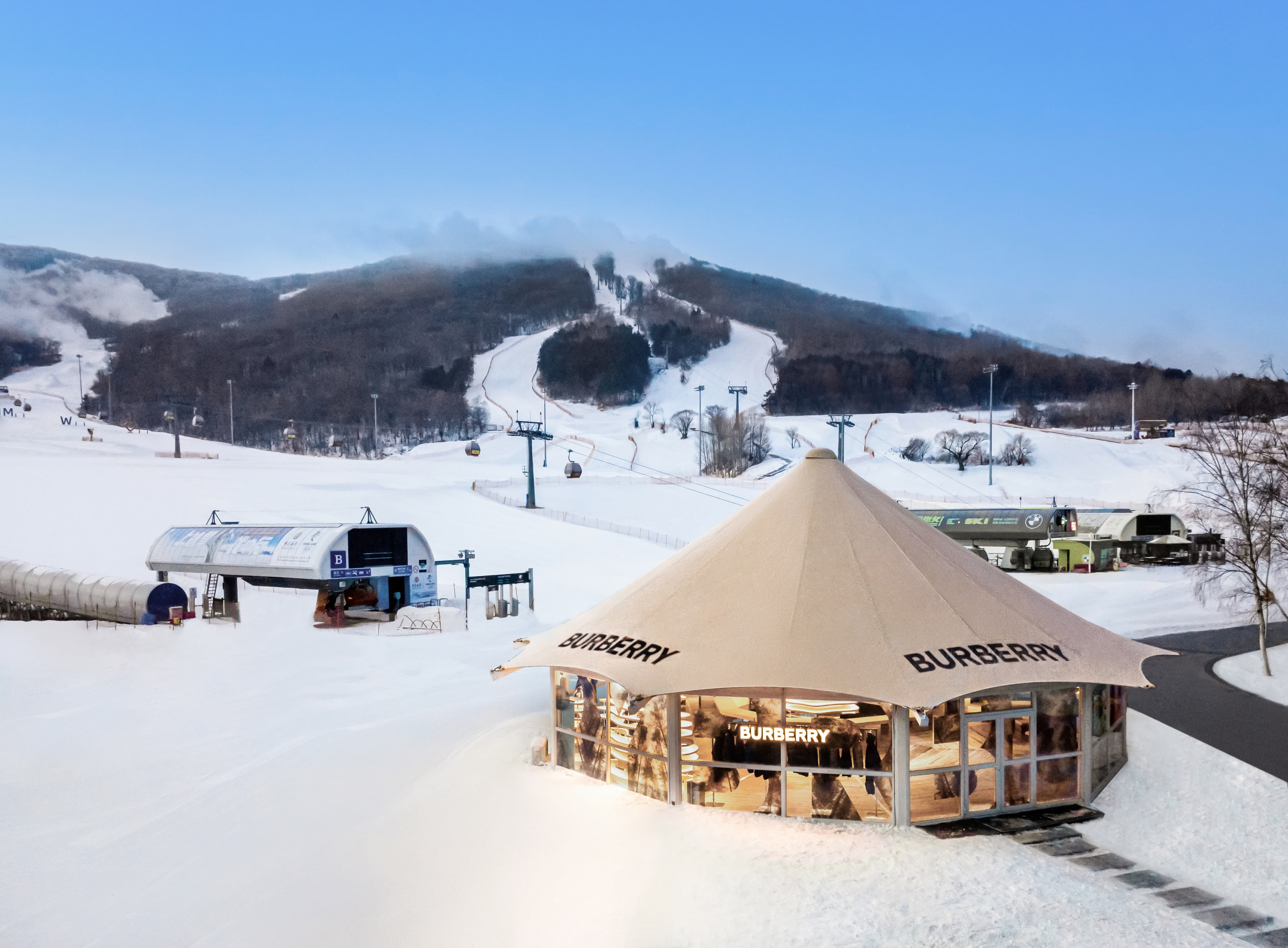 Circular Burberry pop-up shop on a snowy mountain with ski slopes and chairlifts behind.