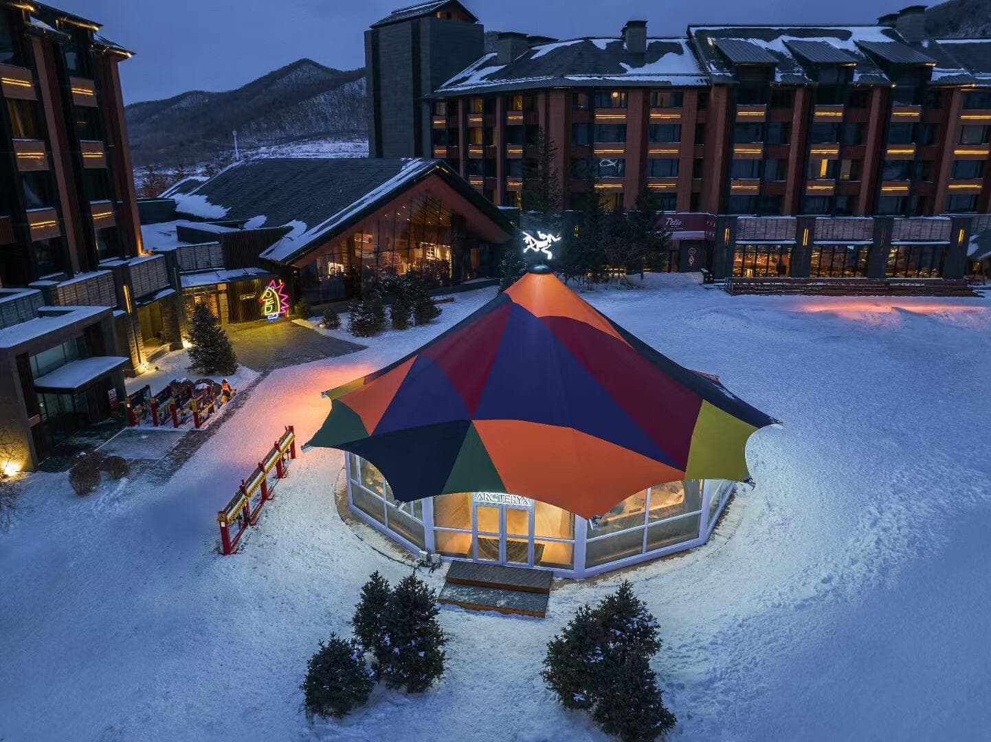 Vibrant multi-colored Arc'teryx tent illuminated in a snowy mountain resort village at night.